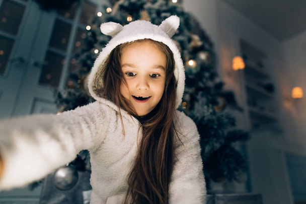 Shocked little girl opening a gift at home in the living room - Photo, image
