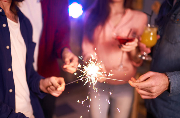 Group of friends having fun with sparklers. young people laugh. celebrating New Year together. Group of beautiful young people in Santa hats. Blur Background - Фото, изображение