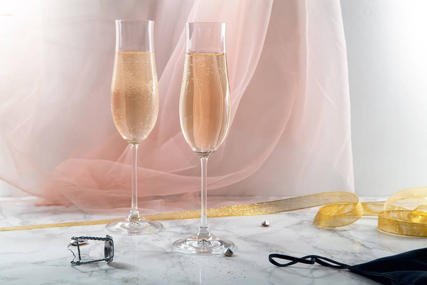Two flute glasses with champagne on marble background. Pink transparent fabric. Soft light. Horizontal composition - Photo, Image