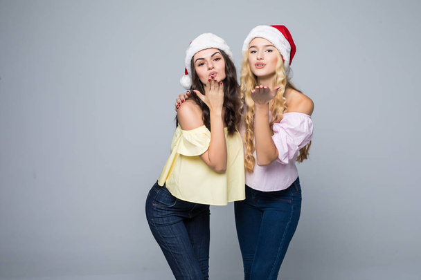 Porträt von zwei schönen glücklichen Frauen mit Weihnachtsmannhüten, die auf weißem Hintergrund isoliert ihren Spaß haben - Foto, Bild