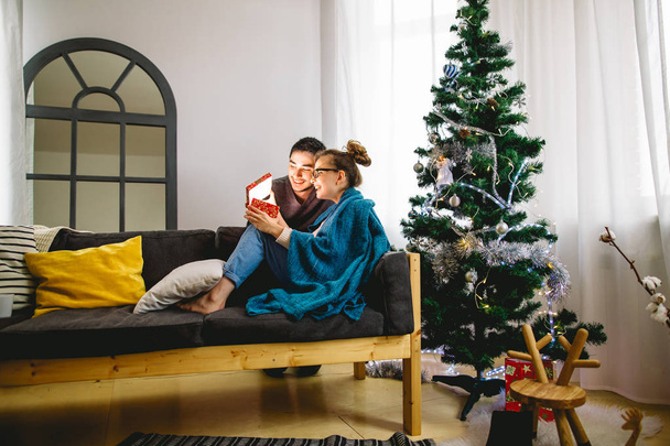 Mujer joven con marido mirando regalo de Navidad
 - Foto, Imagen