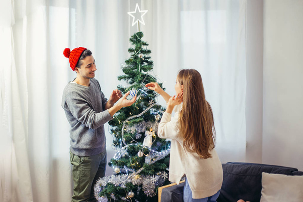 jovem casal feliz decorando uma árvore de Natal. Luz natural, foco seletivo
 - Foto, Imagem