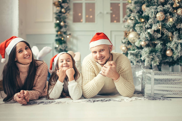 family with Santa hat lying near Christmas tree, holiday celebration concept - Foto, afbeelding