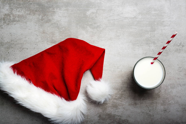 Red santa hat and a glass of milk on a gray concrete table - Photo, Image