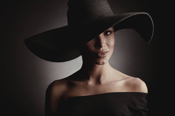 Dark studio portrait of elegant sexy woman in black wide hat and black dress.  - Фото, зображення