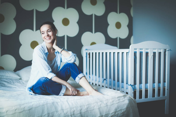 Young woman sitting on the bed near childrens cot. Young mom - Foto, Bild