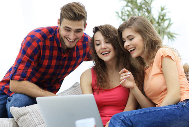Studentengruppe blickt auf einen Laptop-Bildschirm und sitzt auf der Couch - Foto, Bild