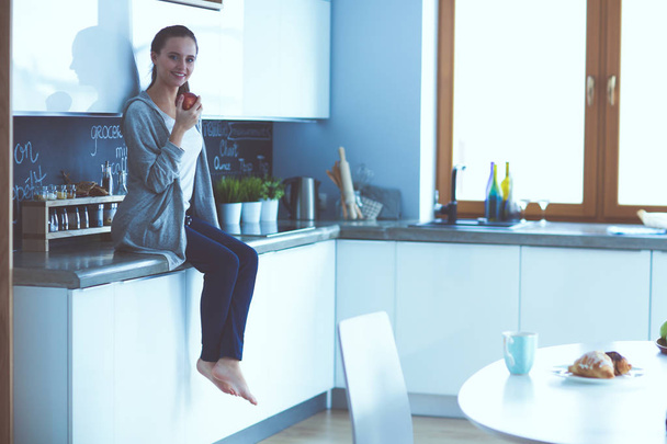 Woman using mobile phone sitting in modern kitchen. - Φωτογραφία, εικόνα
