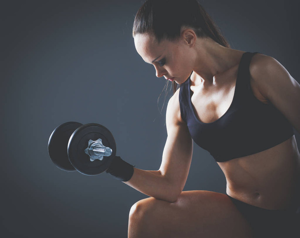 Muscular young woman standing on gray background. Muscular young woman. beautiful girl pumps muscles - Fotó, kép