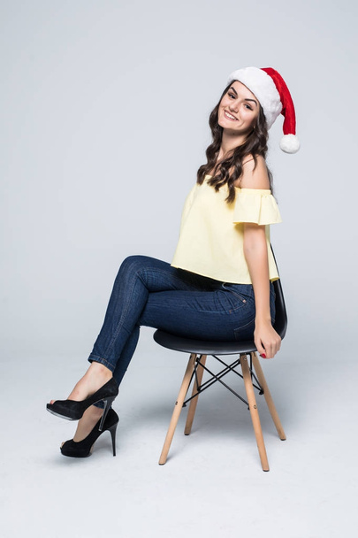 счастливая женщина в шляпе Санта-Клауса с подарочной коробкой сидя в кресле изолированы на белом фоне
 - Фото, изображение
