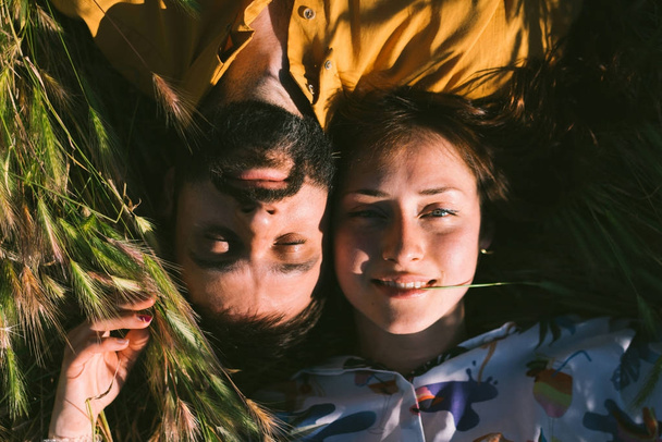 A romantic couple is enjoying warm sunny summer day while lying down amidst the meadow. A man and a woman in love are spending the weekend outdoors. Portrait of a young couple just married. - Foto, Imagem