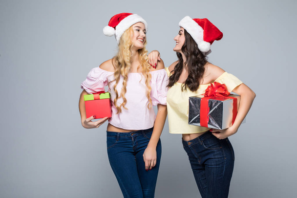 Noel Baba şapkaları beyaz arka plan üzerinde duran hediye kutuları ile iki mutlu kadın - Fotoğraf, Görsel
