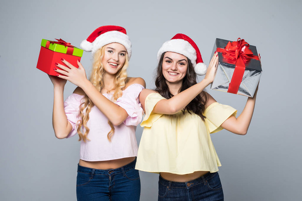 Twee gelukkige vrouwen in santa hoeden met geschenkdozen permanent op witte achtergrond - Foto, afbeelding