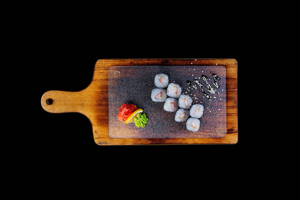 klassische Sushi-Rolle mit Garnelen auf einem Holzbrett. Ansicht von oben. isoliert auf schwarzem Hintergrund - Foto, Bild