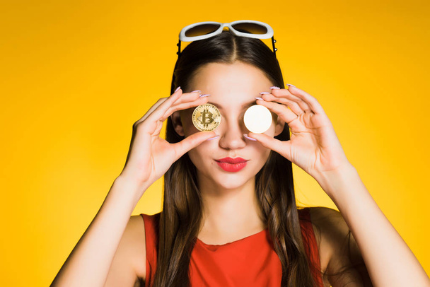 on a yellow background, a young girl is holding golden bitcoins in her hands, smiling - Fotografie, Obrázek