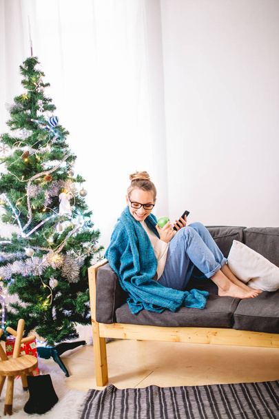 woman browsing on her smartphone, while sitting on a comfy couch - Foto, Imagen