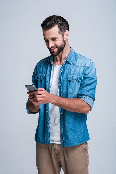 Message to friend. Handsome young man using phone with smile while standing againstwhite background - 写真・画像
