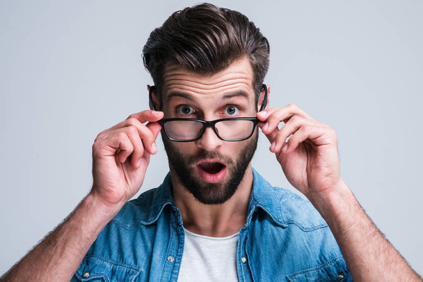 ¡Dios mío! Retrato de un joven guapo ajustando sus gafas y mirando a la cámara mientras está parado sobre un fondo blanco
 - Foto, Imagen
