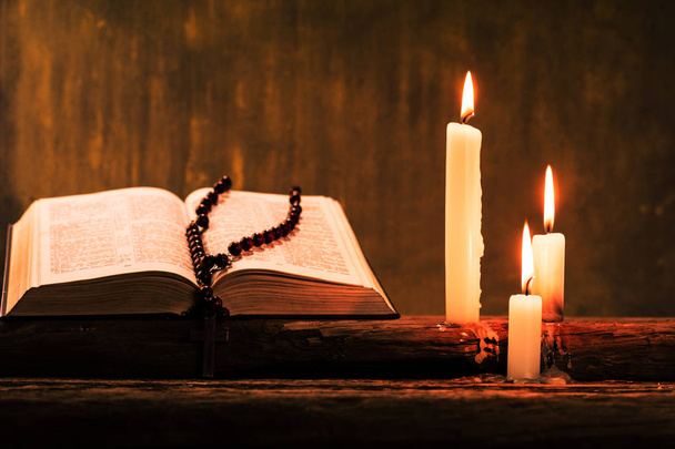 Crucifijo bíblico y cuentas con una vela en una mesa de madera de roble viejo. Hermoso fondo de oro.Concepto de religión
. - Foto, Imagen