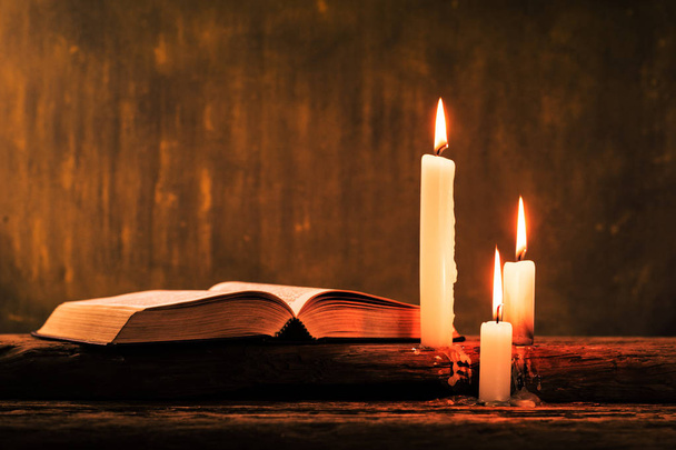 Bibelkruzifix und Perlen mit Kerze auf einem alten Eichentisch. schöner goldener Hintergrund. Religionskonzept. - Foto, Bild