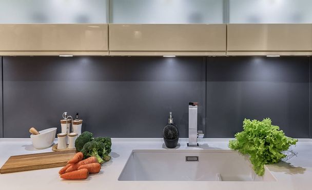 Cucina moderna in stile high-tech con porte scorrevoli al posto del grembiule. Insalata fresca, carote, cavolo Broccoli si trovano sul piano di lavoro accanto al lavandino
. - Foto, immagini