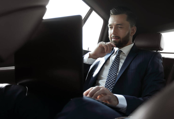 businessman working with laptop and looking out the window of a car - Photo, image