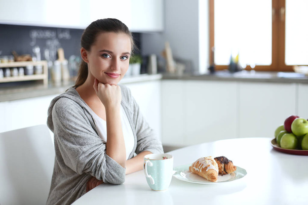 Vrouw het drinken van thee met zoete croissant aan de keukentafel. - Foto, afbeelding