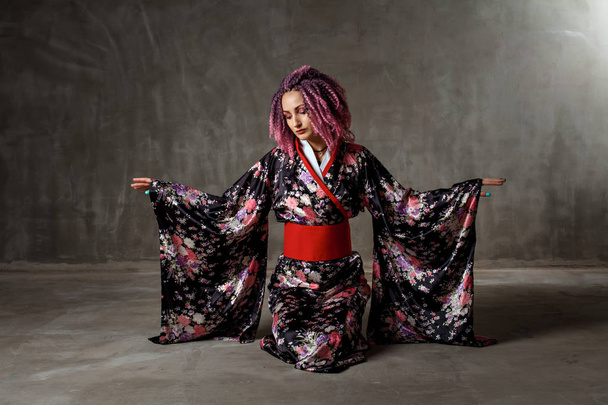 young girl with pink, curly hair in a colored kimono on a black background - Photo, Image