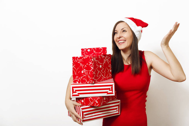 Bella caucasica giovane donna felice con affascinante sorriso vestito in abito rosso e cappello di Natale contenente scatole regalo su sfondo bianco. Santa ragazza con presente isolato. Concetto vacanza di Capodanno 2018
 - Foto, immagini