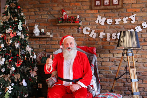 Energetic Santa Claus raises thumb up, sitting on armchair in fe - Photo, Image
