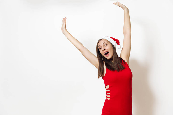 Mulher feliz muito caucasiano jovem com sorriso encantador vestindo vestido vermelho e chapéu de Natal estendendo as mãos isoladas no fundo branco. Santa menina. Férias de Ano Novo 2018. Espaço de cópia para propaganda
 - Foto, Imagem