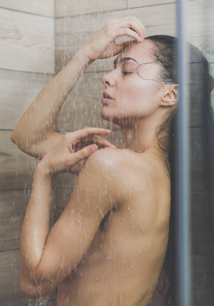 Young beautyful woman under shower in bathroom. - Фото, зображення