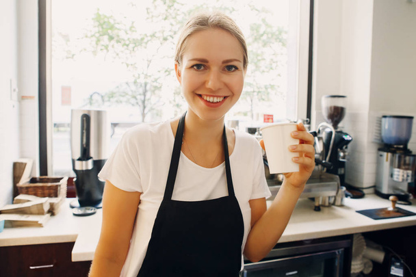 Portrait d'heureuse belle jeune femme souriante caucasienne barista buvant dans une tasse en papier. Personne se reposant relaxant sur le lieu de travail
 - Photo, image