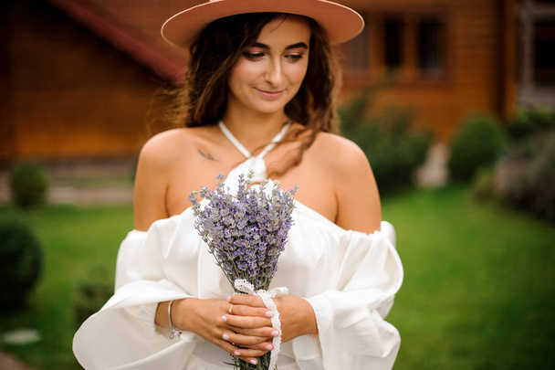 Lovely curly woman dressed in white dress with bouquet of lavender - Foto, Bild
