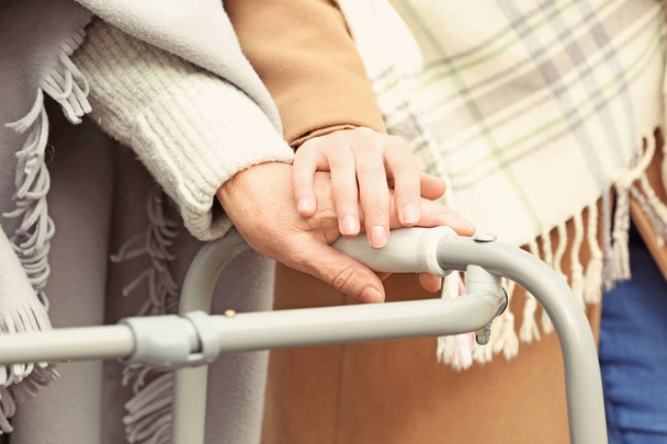 Senior woman with walking frame and young caregiver in park, closeup - Foto, Imagen