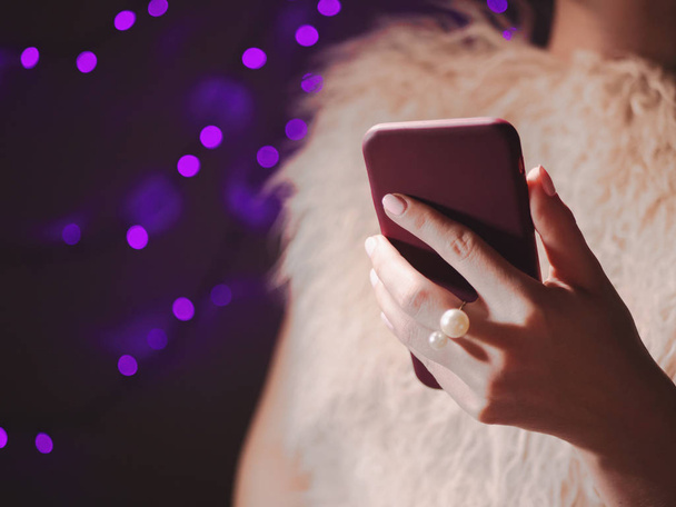 Close-up image of female hands using smartphone at night with bokeh holiday Christmas lights, searching or social networks concept, hipster typing sms message to his friends - Photo, Image