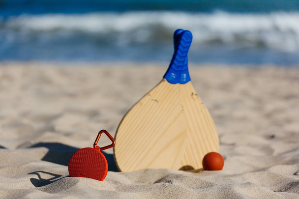 Draadloze draagbare luidspreker en beach tennisrackets op het strand - Foto, afbeelding