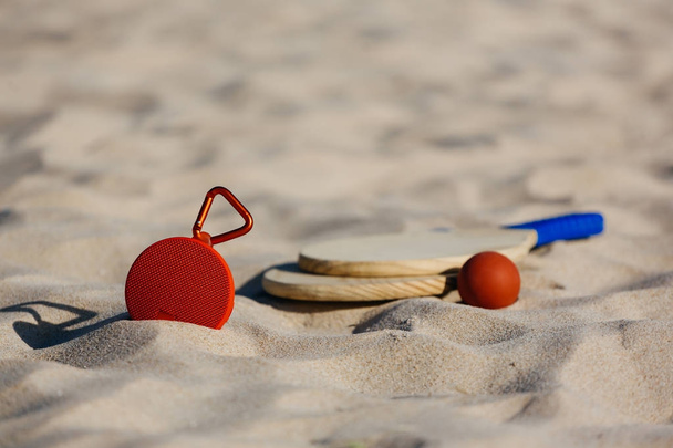 Altavoz inalámbrico portátil y raquetas de tenis de playa en la playa
 - Foto, imagen