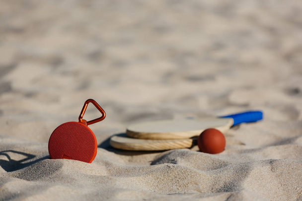 Беспроводной портативный динамик и пляжные теннисные ракетки на пляже
 - Фото, изображение