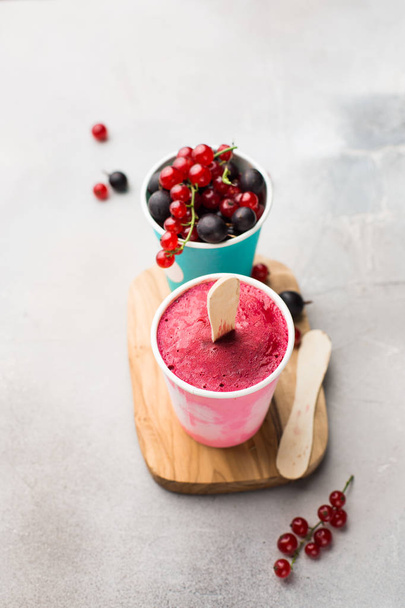 Frozen berry smoothies in bright paper cups on a light gray concrete background with fresh red currant and black gooseberry.place for text. flat lay, top view - Foto, imagen