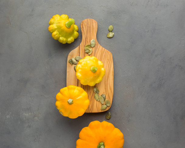 Маленькие апельсиновые сквоши (тыквы) на деревянной доске на бетонном светлом фоне с семенами
.  - Фото, изображение