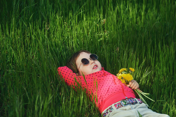 ritratto ravvicinato di una bella bambina. il bambino gioca con i fiori sdraiato sull'erba
 - Foto, immagini