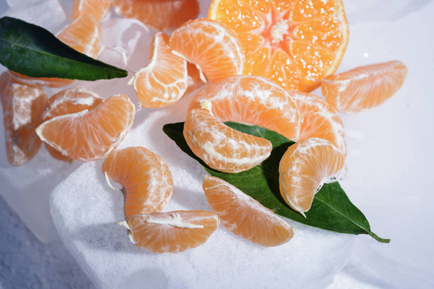 Vers oranje fruit van de Mandarijn met groene bladeren zijn bevroren op koude blauw ijs - Foto, afbeelding
