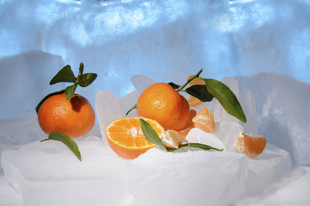 Vers oranje fruit van de Mandarijn met groene bladeren zijn bevroren op koude blauw ijs - Foto, afbeelding