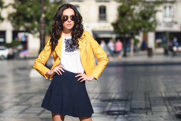 Outdoor waist up fashion portrait of young beautiful sensual woman wearing  stylish leather cap, trendy yellow sunglasses, sexy lace bra, tartan blazer,  posing in street of the city. Copy, empty space Stock