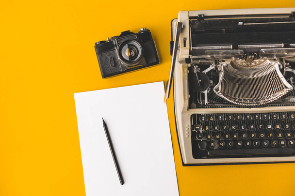 Old typewriter, A Vintage Film Camera, A Sheet Of Paper And A Pencil On A Yellow Background, Top View. Creative concept - Foto, afbeelding