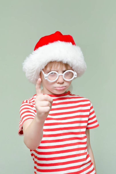 Gloomy Angry boy in a santa hat threatens finger - Photo, Image
