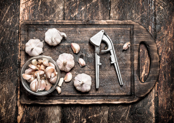 Fragrant garlic with a press tool on a wooden Board. On rustic background. - Zdjęcie, obraz