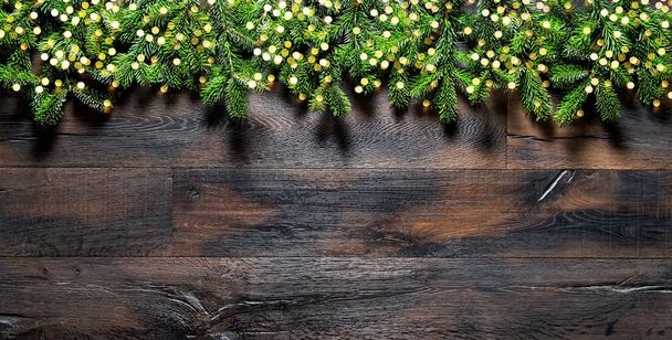 Christmas tree branches golden lights dark wooden background - Фото, изображение