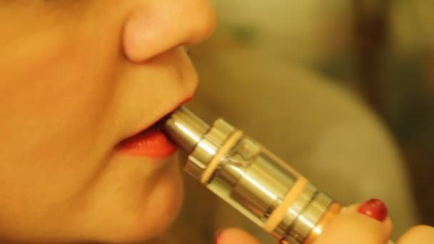 La chica fuma un vaporizador electrónico de cigarrillos y libera vapor de humo de su boca
. - Metraje, vídeo